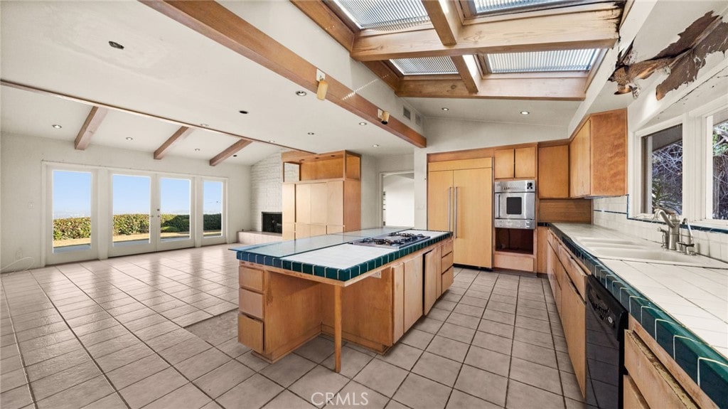 kitchen with vaulted ceiling with skylight, stainless steel gas cooktop, light tile patterned floors, tile countertops, and dishwasher