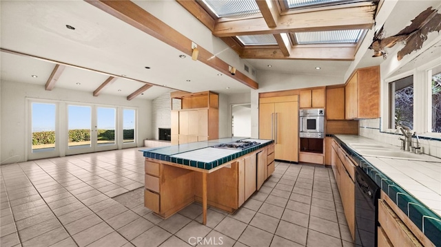 kitchen with vaulted ceiling with skylight, stainless steel gas cooktop, light tile patterned floors, tile countertops, and dishwasher