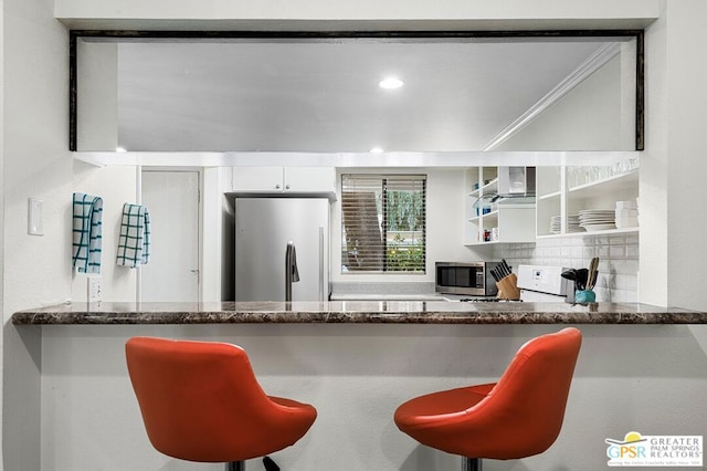 kitchen featuring a breakfast bar, backsplash, stainless steel appliances, and white cabinetry