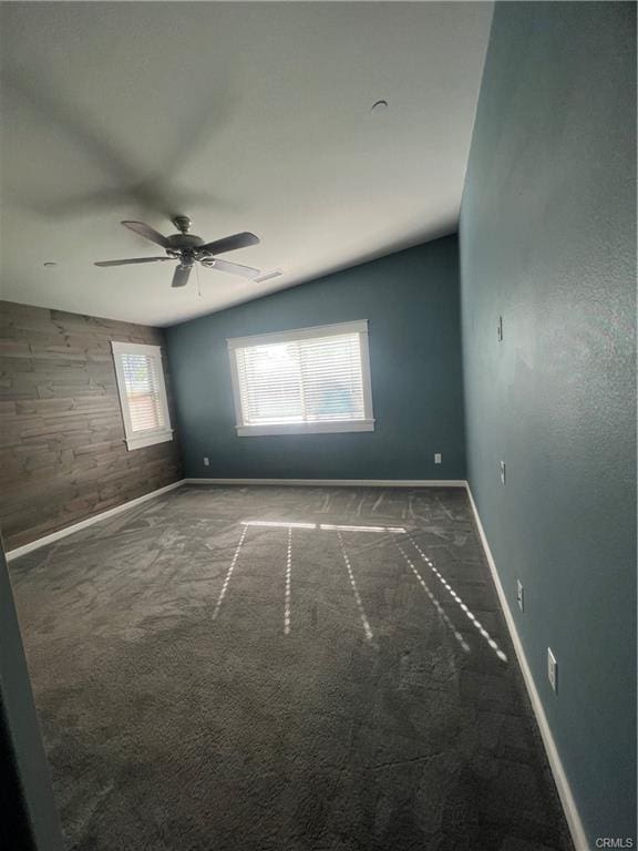 carpeted spare room with lofted ceiling, ceiling fan, and wooden walls