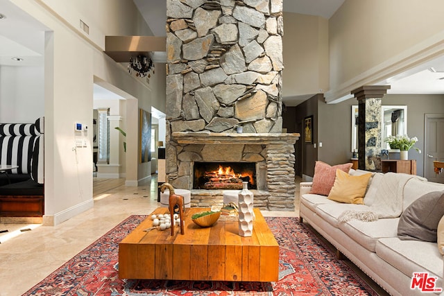 living room featuring a towering ceiling, decorative columns, and a stone fireplace