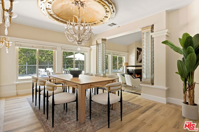 dining space with a tray ceiling, ornate columns, and light wood-type flooring