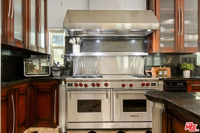 kitchen featuring backsplash, range with two ovens, dark stone countertops, and wall chimney range hood