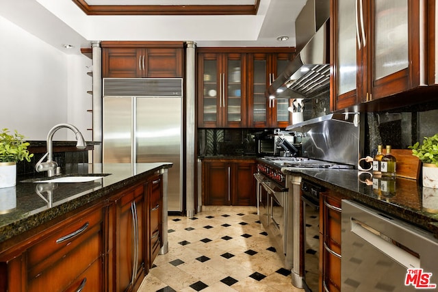 kitchen featuring backsplash, wall chimney exhaust hood, sink, high quality appliances, and dark stone countertops