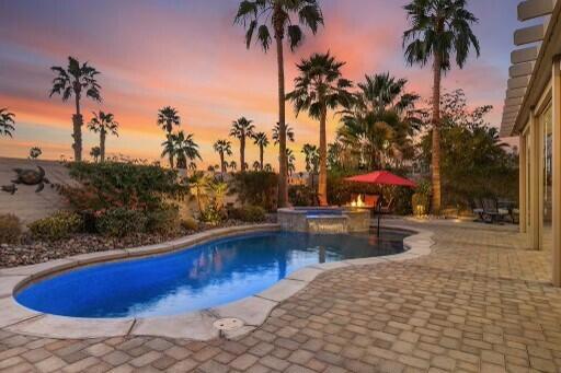 pool at dusk with a patio area and an in ground hot tub