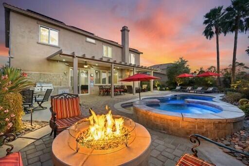 pool at dusk with a patio area, an outdoor fire pit, and an in ground hot tub