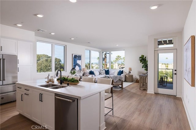 kitchen with appliances with stainless steel finishes, sink, light hardwood / wood-style flooring, white cabinetry, and an island with sink