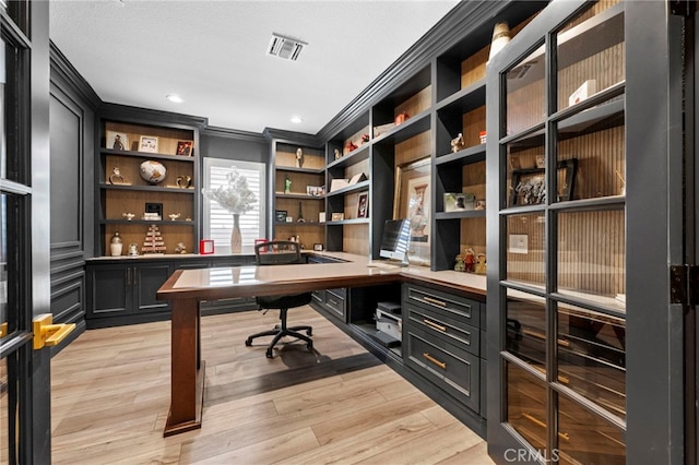 home office with built in desk, built in features, light hardwood / wood-style flooring, and ornamental molding