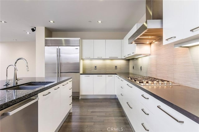 kitchen with appliances with stainless steel finishes, sink, wall chimney range hood, white cabinets, and dark hardwood / wood-style floors