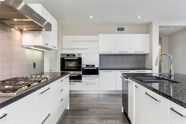 kitchen featuring backsplash, white cabinetry, stainless steel appliances, and wall chimney range hood