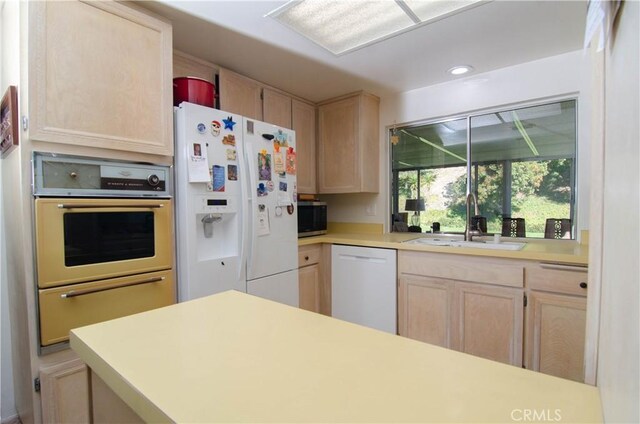 kitchen featuring light brown cabinetry, sink, and white appliances