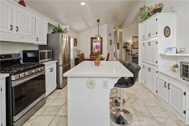 kitchen with appliances with stainless steel finishes, a kitchen island, white cabinetry, and lofted ceiling