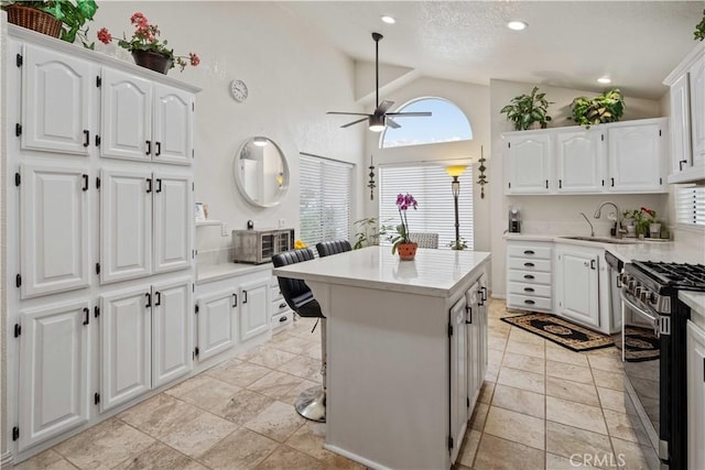 kitchen with gas range, ceiling fan, sink, high vaulted ceiling, and white cabinetry