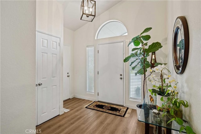 entryway with wood-type flooring, high vaulted ceiling, and an inviting chandelier