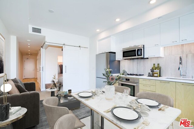 kitchen with backsplash, stainless steel appliances, sink, a barn door, and white cabinetry