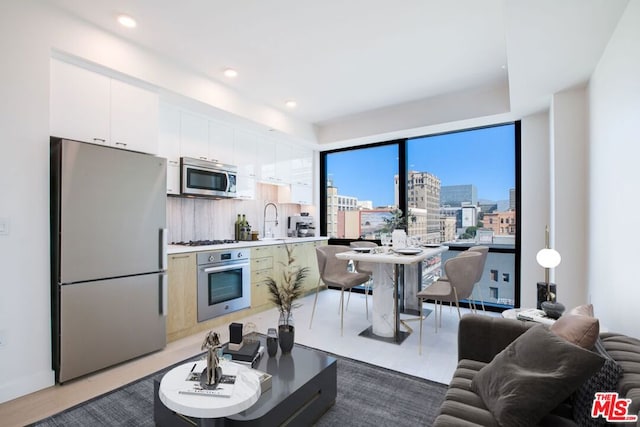 kitchen featuring backsplash, sink, white cabinetry, wood-type flooring, and stainless steel appliances