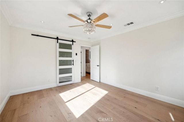 unfurnished bedroom featuring a barn door, light hardwood / wood-style floors, ceiling fan, and ornamental molding