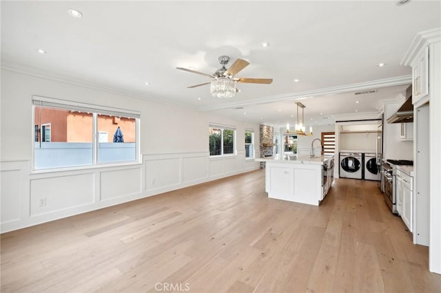 kitchen featuring light wood-type flooring, stainless steel range, decorative light fixtures, a center island with sink, and washing machine and dryer