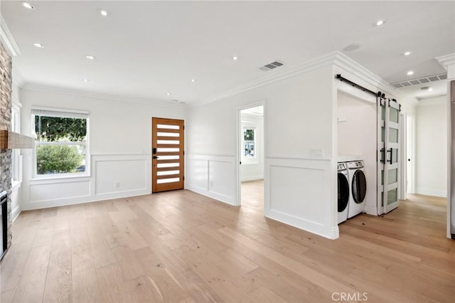 unfurnished living room with a barn door, crown molding, washer and clothes dryer, and light hardwood / wood-style floors