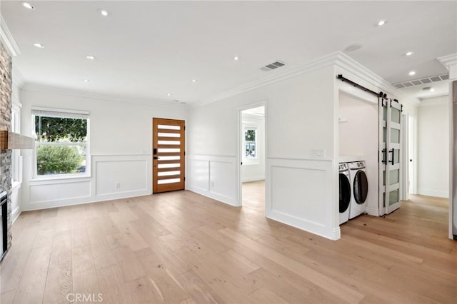 3821 S Muirfield Rd, Los Angeles, CA 90008 - unfurnished living room featuring a barn door, light wood-style flooring, washer and dryer, a stone fireplace, and ornamental molding