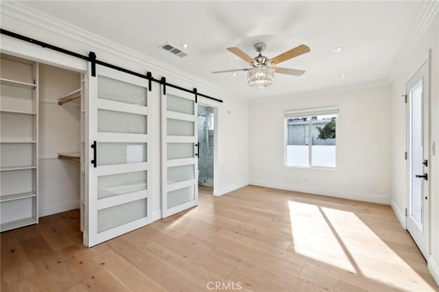 unfurnished bedroom with ornamental molding, ceiling fan, a barn door, light hardwood / wood-style flooring, and a closet