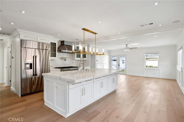 kitchen featuring white cabinets, stainless steel built in fridge, wall chimney exhaust hood, and a center island with sink