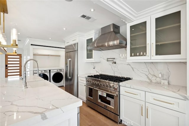 kitchen with light stone countertops, high end appliances, wall chimney range hood, decorative light fixtures, and separate washer and dryer