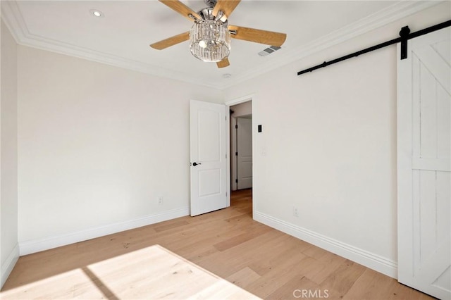 empty room featuring ceiling fan, a barn door, wood-type flooring, and crown molding