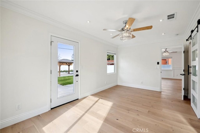 spare room featuring a barn door, light hardwood / wood-style flooring, ceiling fan, and ornamental molding