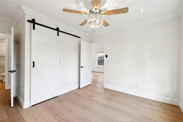 unfurnished bedroom with a barn door, ceiling fan, light hardwood / wood-style floors, and ornamental molding