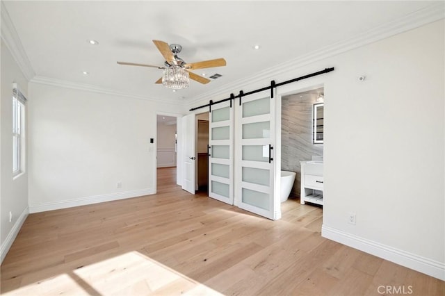 unfurnished bedroom with ensuite bath, ceiling fan, crown molding, a barn door, and light hardwood / wood-style flooring