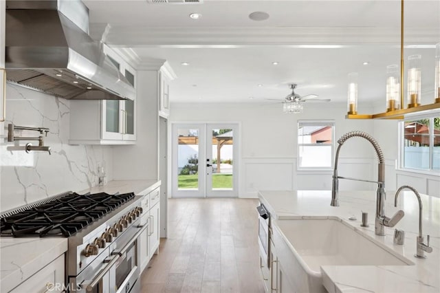 kitchen featuring backsplash, white cabinetry, wall chimney exhaust hood, and light stone counters