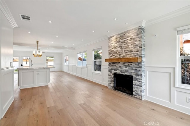 unfurnished living room featuring ornamental molding, sink, light hardwood / wood-style flooring, a chandelier, and a stone fireplace