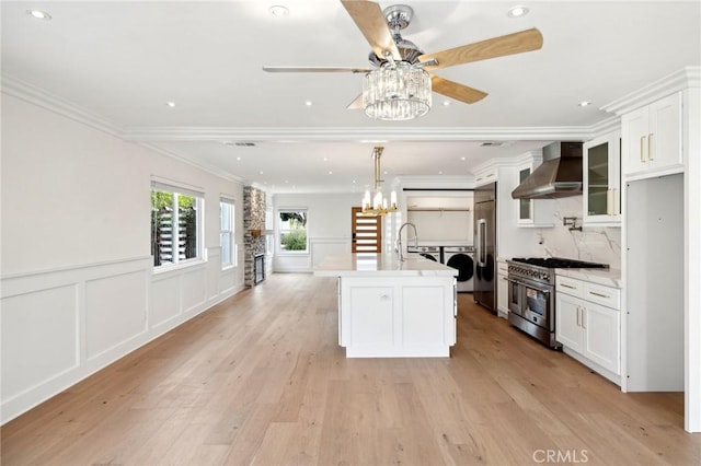 kitchen featuring washing machine and clothes dryer, high end appliances, white cabinetry, wall chimney exhaust hood, and light wood-type flooring