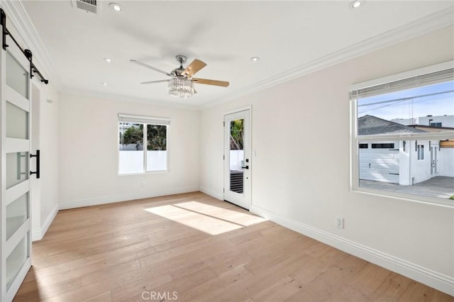 empty room with a barn door, crown molding, ceiling fan, and light wood-type flooring