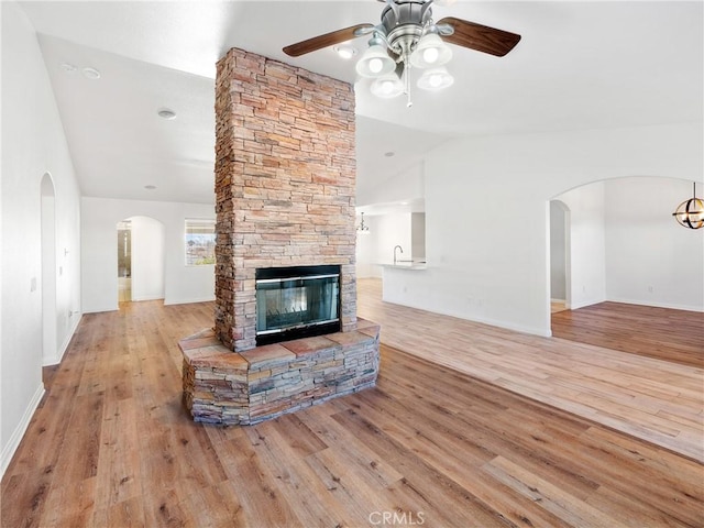 living room with light hardwood / wood-style floors, vaulted ceiling, ceiling fan, and a stone fireplace