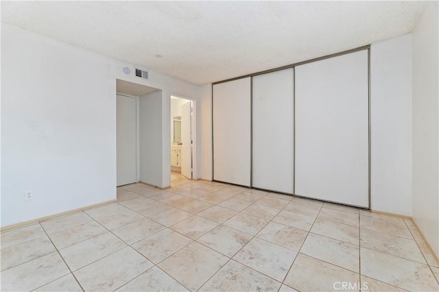 unfurnished bedroom with ensuite bath, light tile patterned flooring, and a closet