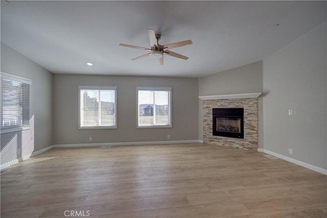 unfurnished living room featuring light wood-type flooring, a stone fireplace, and ceiling fan