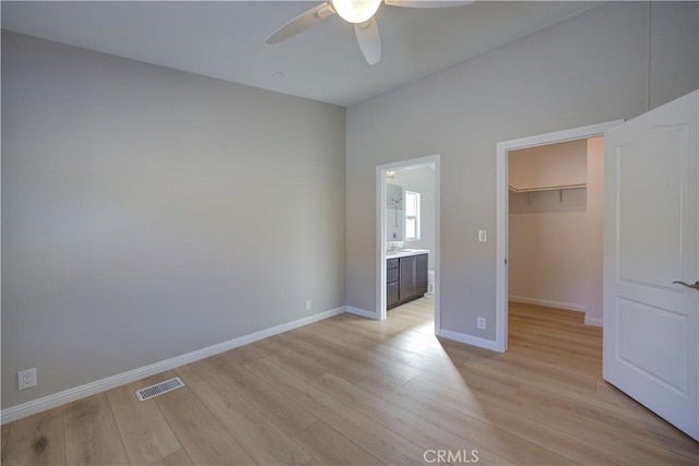 unfurnished bedroom featuring a walk in closet, ensuite bath, light hardwood / wood-style flooring, ceiling fan, and a closet