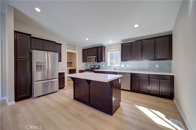 kitchen with light wood-type flooring, dark brown cabinetry, stainless steel appliances, a kitchen island, and a breakfast bar area