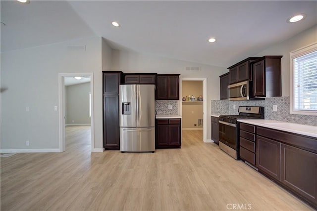 kitchen with backsplash, stainless steel appliances, vaulted ceiling, and light hardwood / wood-style floors