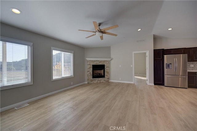 unfurnished living room with a stone fireplace, ceiling fan, vaulted ceiling, and light wood-type flooring