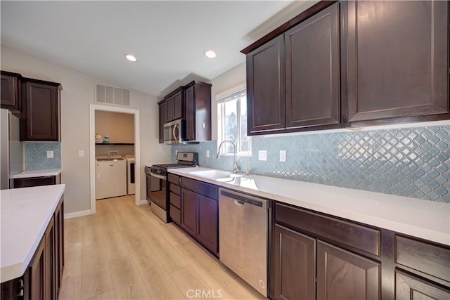 kitchen featuring sink, stainless steel appliances, decorative backsplash, washer and dryer, and light wood-type flooring