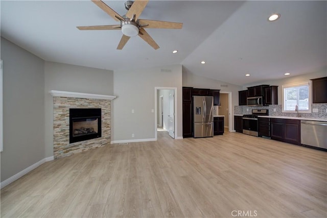 unfurnished living room featuring ceiling fan, sink, light hardwood / wood-style flooring, a fireplace, and lofted ceiling