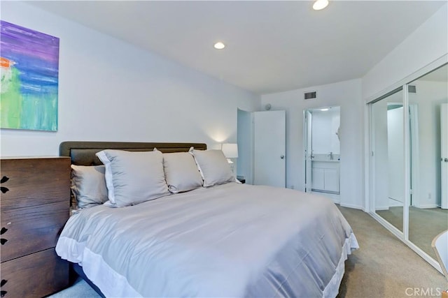 bedroom with ensuite bathroom, a closet, and light carpet