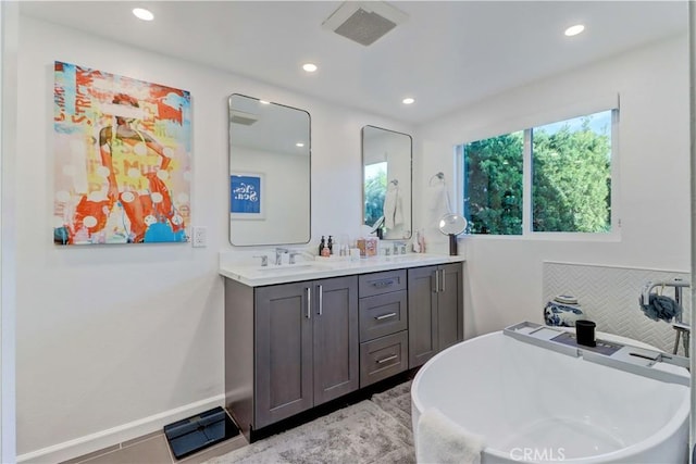 bathroom with a tub to relax in, vanity, and tile patterned floors