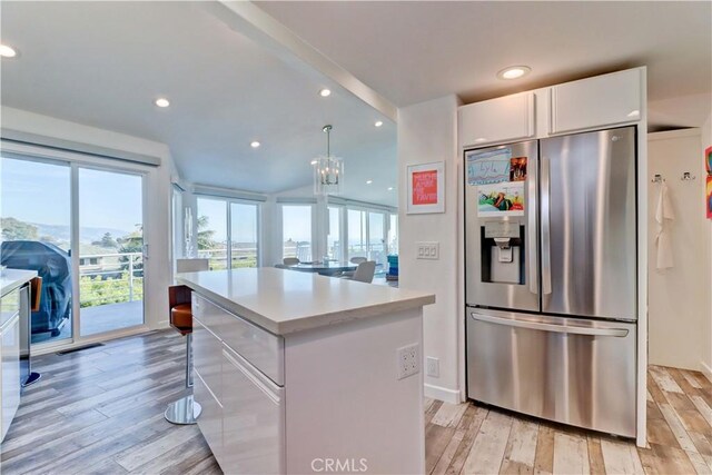 kitchen with a kitchen island, pendant lighting, stainless steel refrigerator with ice dispenser, white cabinetry, and a healthy amount of sunlight