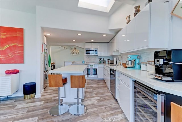 kitchen featuring white cabinetry, a kitchen bar, stainless steel appliances, backsplash, and beverage cooler