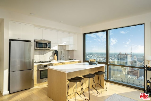 kitchen with a kitchen bar, appliances with stainless steel finishes, a kitchen island, sink, and white cabinetry