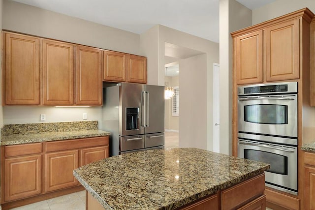 kitchen featuring light tile patterned floors, light stone countertops, appliances with stainless steel finishes, and a center island